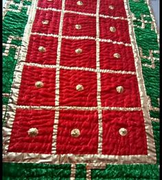 a red and green quilted table runner with gold dots on it's edges