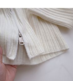 a hand holding a white sweater with a zipper