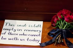 a bouquet of red roses sitting on top of a wooden table next to a sign