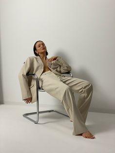 a woman sitting in a chair with her legs crossed and wearing a blazer and pants