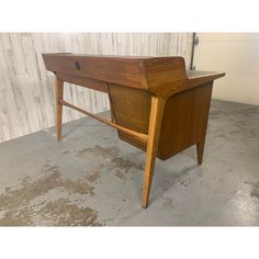 a wooden desk sitting on top of a cement floor in front of a white wall