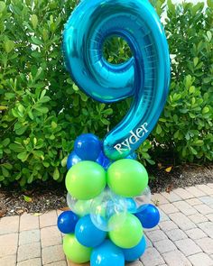 a blue and green balloon with the number nine on it in front of some bushes