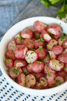 a white bowl filled with red potatoes on top of a blue and white table cloth