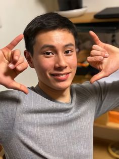 a young man is making the peace sign with his hands while sitting in front of a computer desk