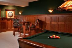 a pool table and chairs in a room with wood paneled walls, darts on the wall