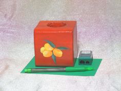 a red box with yellow flowers on it next to a green pen and eraser