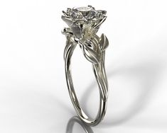 "A dainty 14k white gold ring showing a lotus set with a beautiful diamond or moissanite for your choice. The lotus is surrounded by a composition of leaves giving the ring a very natural look. ★See A Video Of This Amazing Ring Here★ https://youtu.be/WDBLPTtTrnQ Details: SKU: Fle39ww Gem Details: Center Gem: Choose between Moissanite or Natural diamond. Carat Weight: Choose from the \"Weight\" button Color/ Clarity: Moissanite - Forever One 'Charles & Colvard' arrive with the warranty certif Elegant Sterling Silver Flower Ring With Brilliant Cut, Elegant Diamond Solitaire Flower Ring, Elegant Solitaire Diamond Flower Ring, Elegant White Gold Solitaire Flower Ring, Elegant Wedding Flower Ring With Single Diamond, Elegant Flower Ring With Prong Setting, White Gold Solitaire Diamond Flower Ring, Delicate White Gold Diamond Flower Ring, Elegant Solitaire Flower Ring With Round Cut