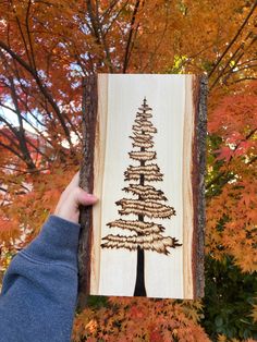 a person holding up a piece of wood with a tree on it in front of some trees