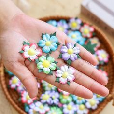 a person's hand holding small flowers in front of a basket full of fake flowers