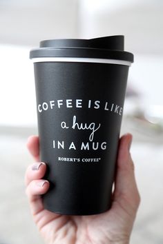 a person holding a coffee cup with the words coffee is like a hug in a mug