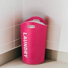 a pink laundry bag sitting on the floor next to a white tiled wall and counter