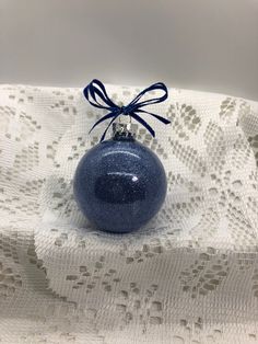 a blue ornament with a bow on top of a white lace table cloth