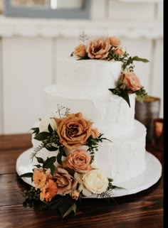 a three tiered white cake with orange flowers on the side and greenery around it