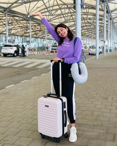 a woman is standing with her luggage at the airport and smiling for the camera while wearing a purple shirt