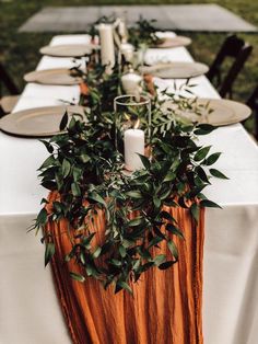 a long table with candles and greenery on it is set for an outdoor dinner