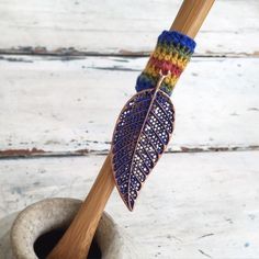 a crocheted leaf is hanging from a wooden stick