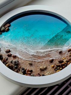 an image of the ocean from inside a round glass window with rocks and pebbles on it