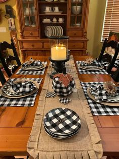 a dining room table set with black and white buffalo checkered placemats, plaid napkins, candlesticks and plates