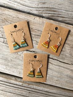 three small earrings with colorful beads hanging from them on a wooden table next to a piece of paper