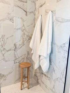 a bathroom with marble walls and white towels hanging on the wall next to a stool