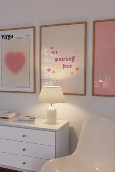 two framed pictures hang on the wall above a white dresser with a lamp in front of it