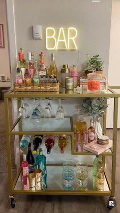 a bar cart filled with lots of bottles and glasses next to a neon sign that says bar