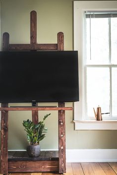 a tv sitting on top of a wooden stand in front of a window with a potted plant next to it