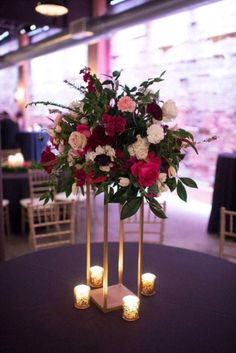 two tall vases with flowers and candles are on a round table in front of chairs