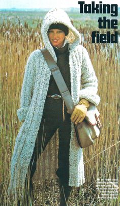 a woman standing in tall grass wearing a white coat and holding a brown handbag