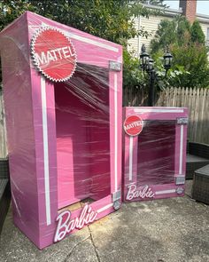 two pink boxes sitting on top of a sidewalk next to each other in front of a fence