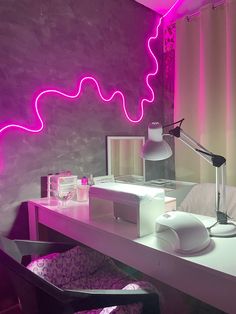 a white desk topped with a computer monitor next to a purple neon light filled wall