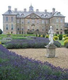 a statue is in the middle of a garden with lavenders and bushes around it