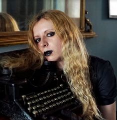 a woman with long blonde hair sitting in front of an old typewriter