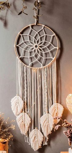 a white dream catcher hanging on the wall next to a vase with flowers in it