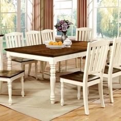 a dining room table with white chairs and a bowl of fruit on top of it