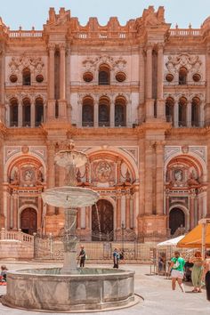 people are standing around in front of an old building with a fountain and umbrellas