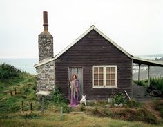 a woman is standing in the doorway of a small house with a chimney next to it