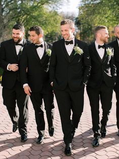 a group of men in tuxedos walking down a brick road together and smiling