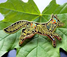 a brooch depicting a fox on a leafy green surface with leaves in the background