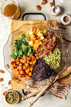 a glass bowl filled with different types of vegetables and nuts on top of a wooden cutting board