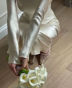 a woman kneeling on the floor holding a flower in her hand and wearing high heeled shoes