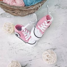 crocheted sneakers and balls of yarn sitting on the floor in front of a basket