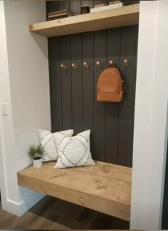 a wooden bench with two white pillows and a brown backpack hanging on the wall behind it