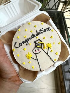 a cake with congratulations written on it sitting in a foam container next to a plant