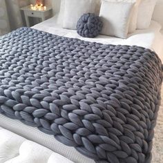 a large gray blanket sitting on top of a bed next to two white pillows in a bedroom