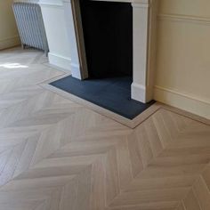 an empty room with a fireplace in the corner and parquet flooring on the other side