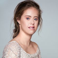 a woman with blue eyes is posing for a photo in front of a gray background