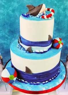 a three tiered cake with blue icing and white frosting, topped with shark decorations