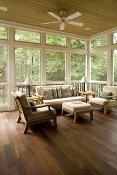 a sun room with wooden floors and large windows on the wall, along with two couches that are facing each other