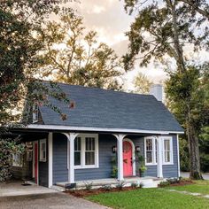 a small blue house with red door and windows in the front yard, surrounded by trees